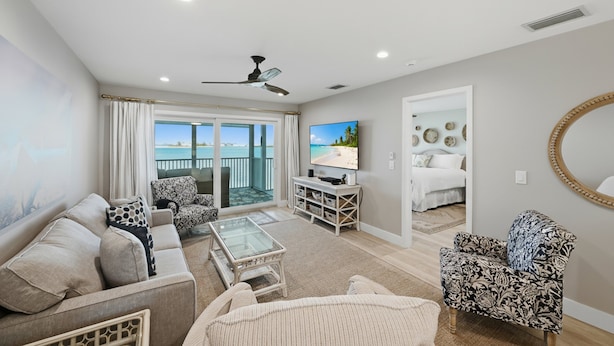 A spacious living room with a balcony, a television, and a cozy seating area. - NEW LOW PRICE - Coastal BG North 82, a spacious 2-bed, 2-bath Boca Grande with stunning Gulf views (Boca Grande)