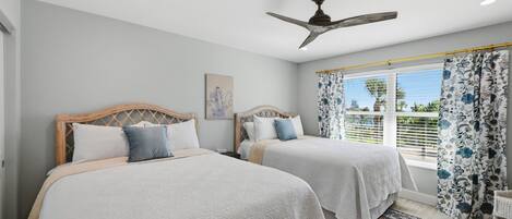 A bedroom with two beds, a ceiling fan, a window with curtains, and a painting on the wall.