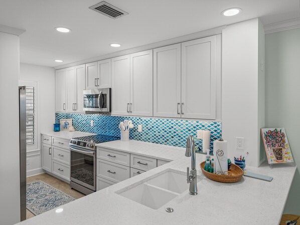 Una cocina moderna con armarios blancos, un microondas de acero inoxidable y un salpicadero azul con diseño.