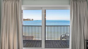 Ein Zimmer mit einer großen Schiebeglastür, die auf einen Balkon mit Blick auf das Meer und eine entfernte Insel führt.