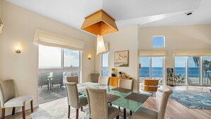 Un'ampia sala da pranzo con tavolo e sedie in vetro, vista sull'oceano e lampadario.
