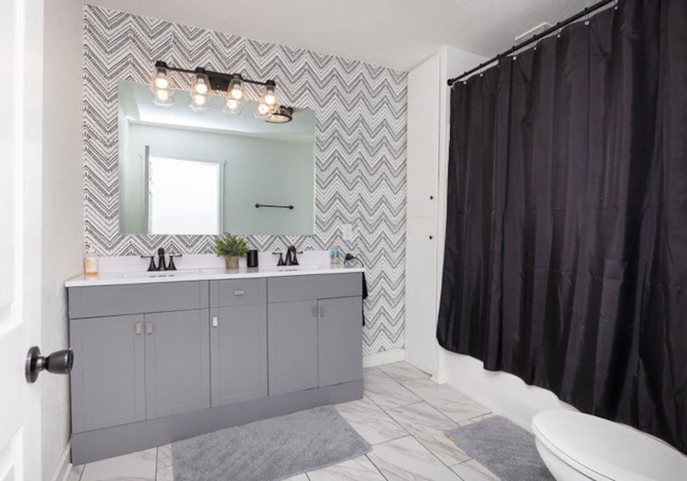 Un baño con tocador gris, un espejo grande y cortina de ducha negra.