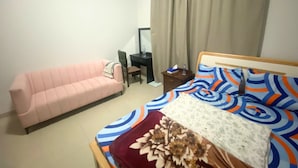 A bedroom with a bed, a pink sofa, a desk, and a chair.