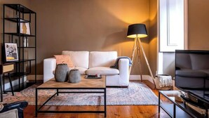 Ein modernes Wohnzimmer mit einem weißen Sofa, einem Couchtisch, einer Stehlampe, einem Bücherregal und einem Fernseher.