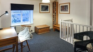 Ein Zimmer mit Fenster, Schreibtisch, Stuhl, Bücherregal und einer Treppe.