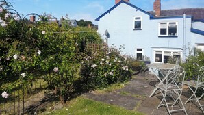 Ein Garten mit einem Metalltisch und Stühlen, einem blauen Haus und einem Rosenbusch.