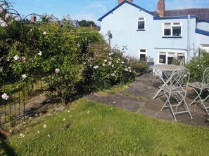 A garden with a metal table and chairs, a blue house, and a rose bush. - 3 bedroom accommodation in Bishops Castle (Bishops Castle)