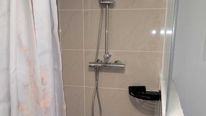 A shower area with a handheld showerhead, a wall-mounted faucet, and a black soap dish.