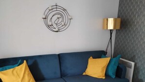 A modern living room with a blue sofa, yellow and teal pillows, a white coffee table, and a decorative wall piece.