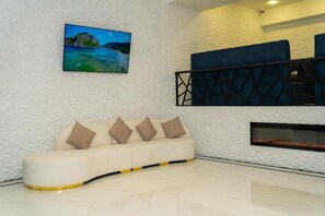 A modern living room with a white textured wall, a beige sofa with cushions, a painting of a landscape, and a fireplace. - Port Marine Hotel (Baku)