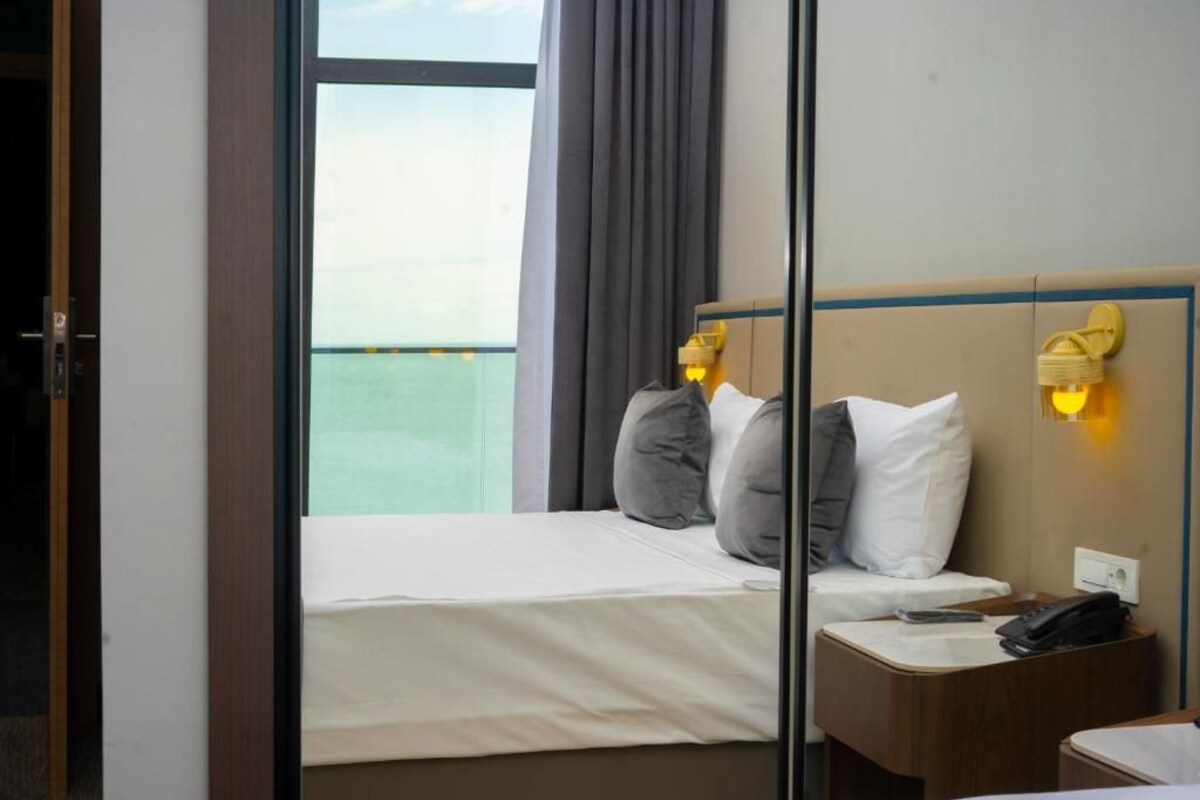 A hotel room with a bed, bedside table, and a view of the sea.