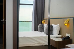 A hotel room with a bed, bedside table, and a view of the sea. - Port Marine Hotel (Baku)