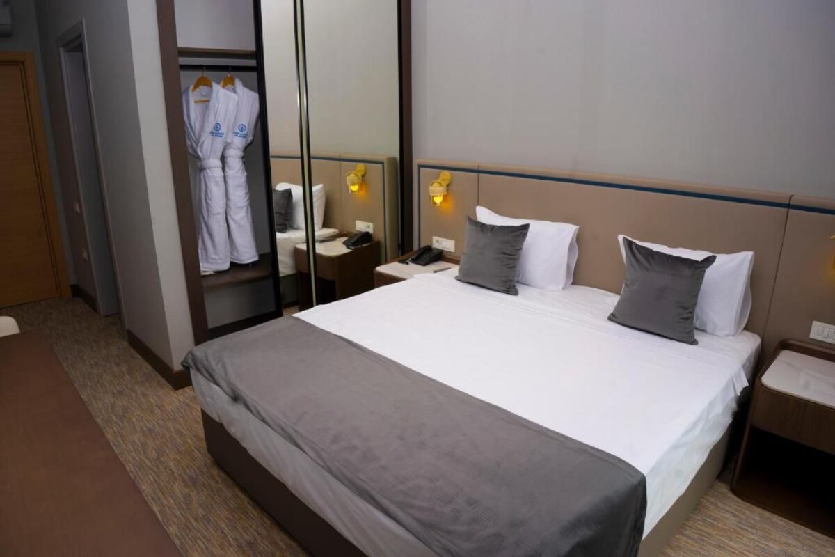A hotel room with a large bed, a bedside table with a lamp, a wardrobe, and a mirror.