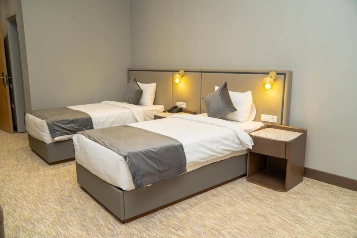 A hotel room with two single beds, each with a pillow and a bedside table.