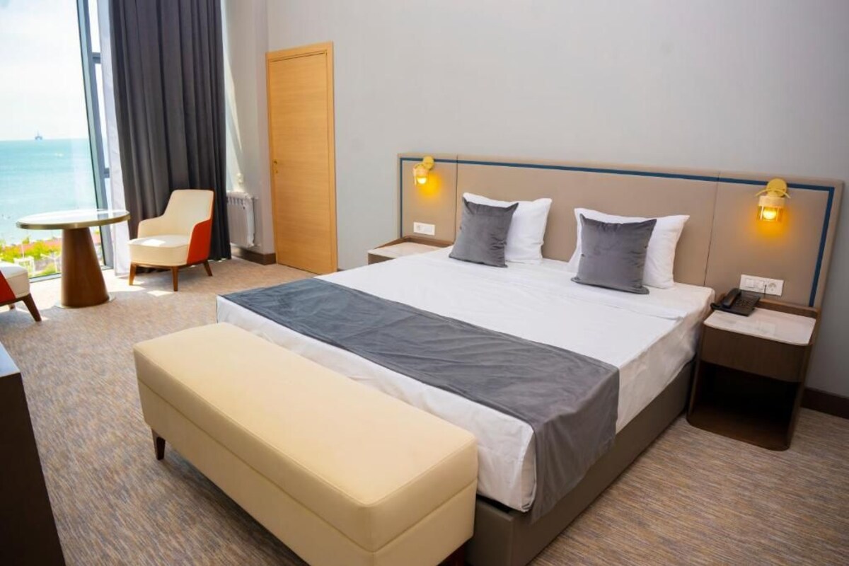 A hotel room with a large bed, bedside tables, a chair, and a view of the sea.