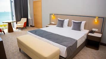 A hotel room with a large bed, bedside tables, a chair, and a view of the sea.