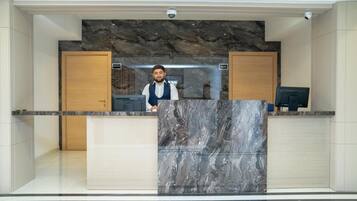 A reception desk with a marble front, wooden cabinets, and a security camera above.