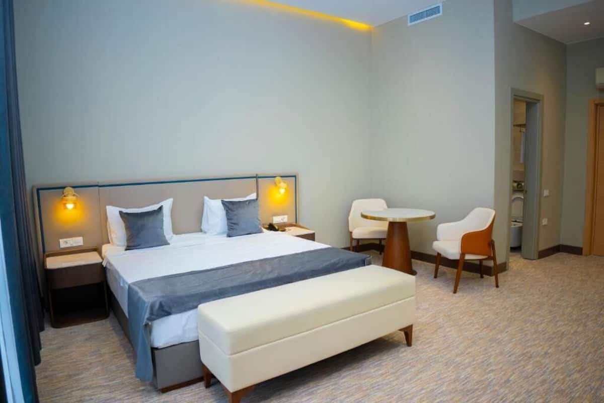 A hotel room with a bed, bedside tables, a bench, a round table, and two chairs.