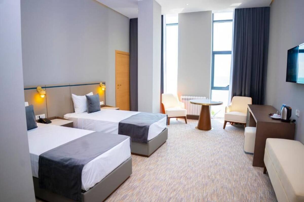A hotel room with two beds, a desk, a chair, a TV, and a large window.