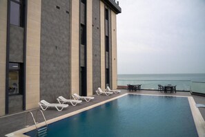 A rooftop pool with lounge chairs and a table, overlooking the sea. - Port Marine Hotel (Baku)