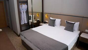 A hotel room with a large bed, a bedside table with a lamp, a wardrobe, and a mirror.