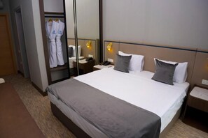A hotel room with a large bed, a bedside table with a lamp, a wardrobe, and a mirror.