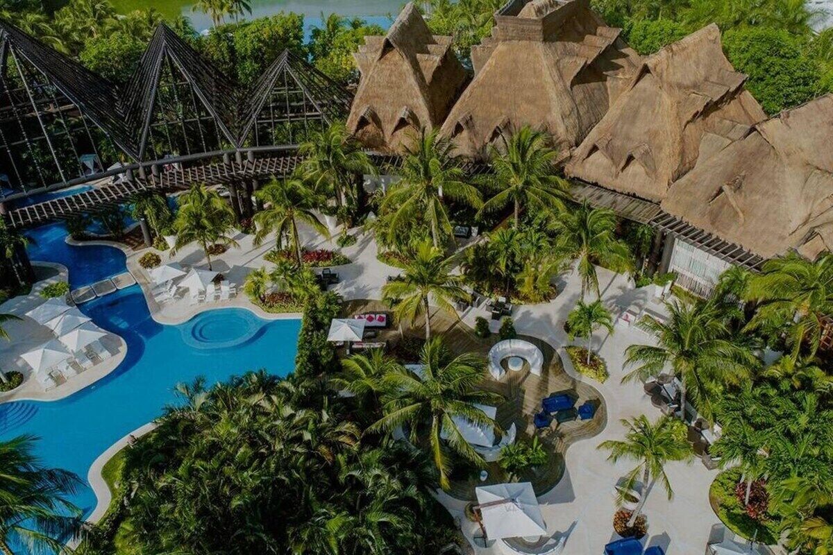 Ein Resort mit großem Swimmingpool, Palmen und strohgedeckten Gebäuden.