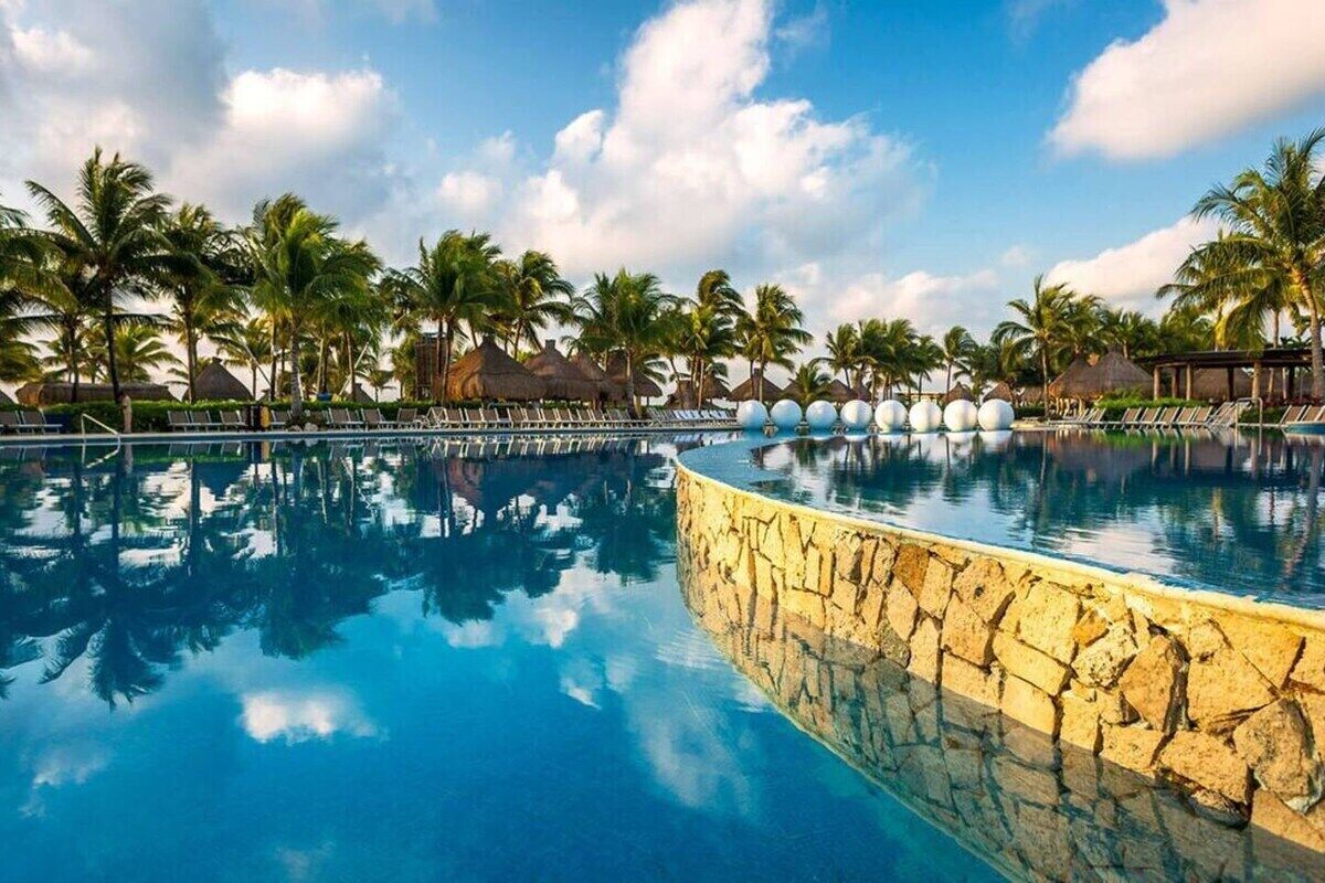 A large, clear swimming pool with lounge chairs and palm trees in the background.