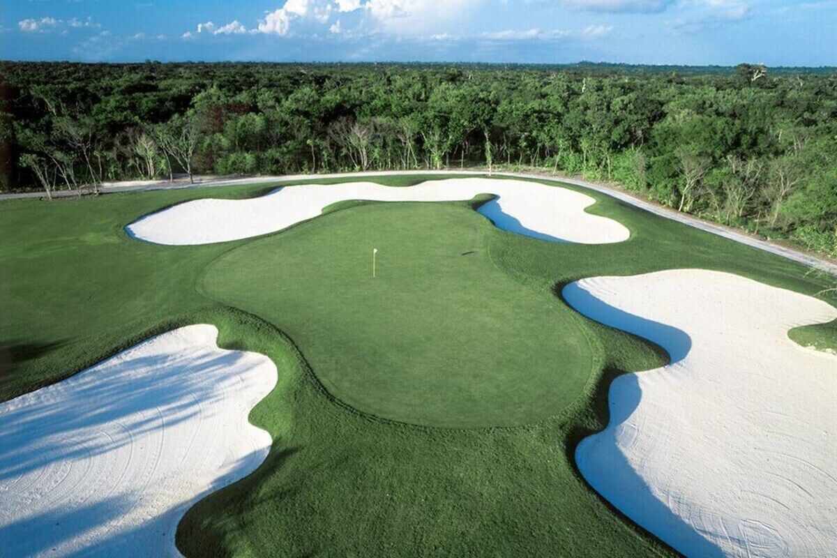 Um campo de golfe com bunkers de areia, uma bandeira e um céu limpo.