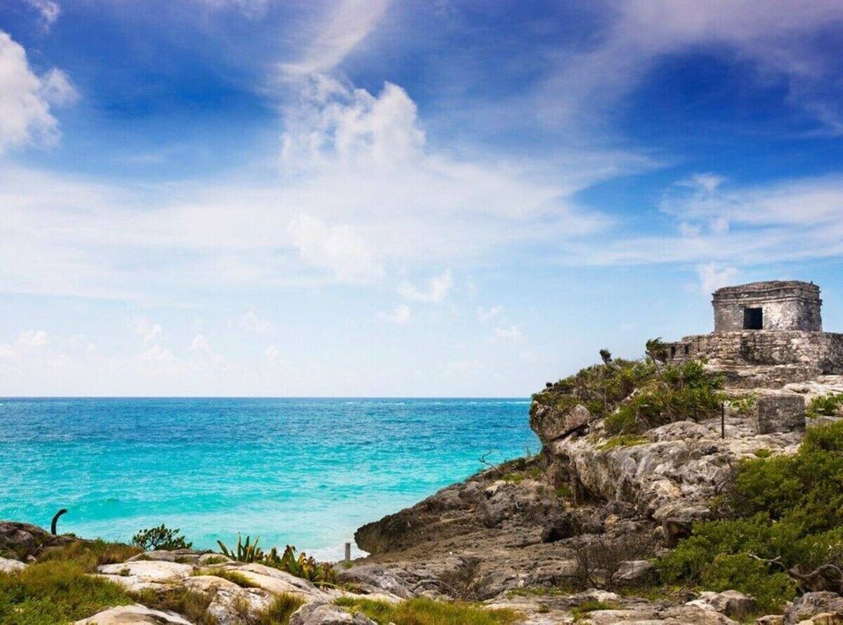 Une vue côtière avec une structure en pierre d’époque, perchée sur une falaise surplombant des eaux turquoise.