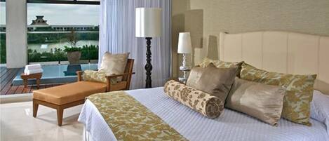 A hotel room with a bed, a chair, a table, and a view of a building and greenery.