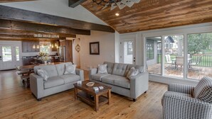 A spacious living room with a wooden ceiling, two grey sofas, a wooden coffee table, and large windows offering a view of the backyard. - Gull Lake Cabin + Bunkhouse with Sandy Beach & Pontoon/Jet Ski availability! (Nisswa)