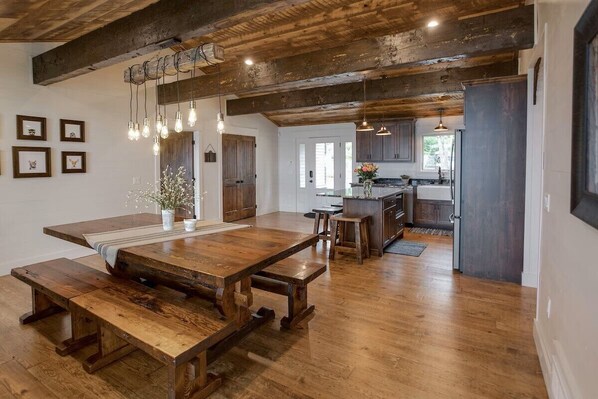 Una cocina rústica con vigas de madera, una gran mesa de madera e iluminación colgante.