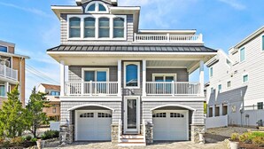A two-story house with a balcony on the upper floor, a garage, and a stone foundation. - Immaculate Pool/Elevator 5 bedroom, 4 bath home w/outdoor living space/fire pit  (Harvey Cedars)