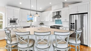 A modern kitchen with white cabinetry, stainless steel appliances, and a central island with bar stools. - Immaculate Pool/Elevator 5 bedroom, 4 bath home w/outdoor living space/fire pit  (Harvey Cedars)