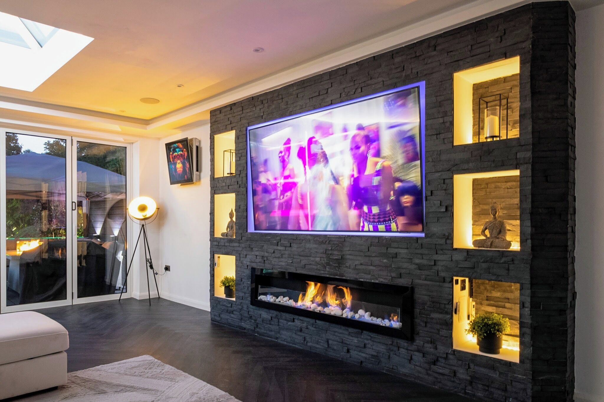 Ein modernes Wohnzimmer mit großem Flachbildfernseher an einer Steinwand, einem Kamin und eingebauten Regalen mit Dekorationselementen.