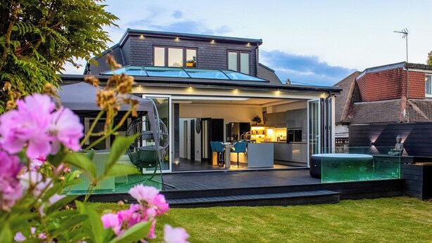 Ein modernes Haus mit überdachter Terrasse, Whirlpool und gepflegtem Rasen.