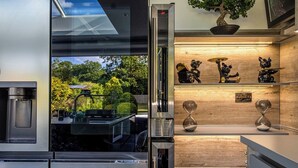 Eine moderne Küche mit Einbaukühlschrank, einer Kaffeemaschine und Blick auf einen Garten durch eine Glastür.