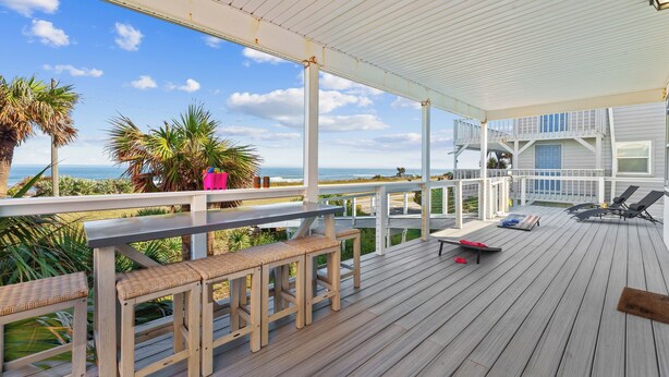 A wooden deck with a railing, benches, and lounge chairs overlooking a coastal view.