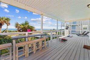 Een houten terras met een leuning, banken en lounge fauteuils, met uitzicht op de kust.