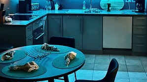 A compact kitchen with dark cabinets, a microwave, a toaster, and a sink. There is a dining table with chairs and a few items on it.