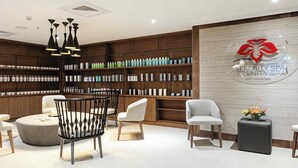 A modern spa reception area with wooden shelving displaying various products, a seating area with chairs, and a logo on the wall.