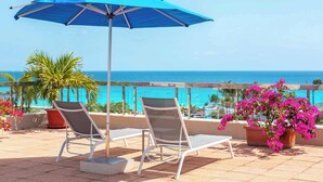 A balcony with two lounge chairs, a blue umbrella, and a view of the ocean.