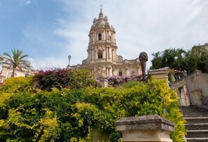 A historic building with a prominent bell tower, surrounded by lush greenery and a stone staircase.
