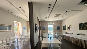 Un espace repas avec des tables et des chaises blanches, un mur en pierre et des tableaux encadr és accrochés aux murs.