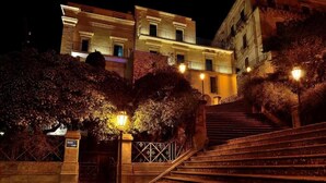 Vue nocturne d’un bâtiment avec un escalier menant à une entrée fermée par un portail.