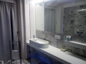 A modern bathroom with a large mirror, a white sink, and a glass shower enclosure. - Hotel San Giorgio (Modica)