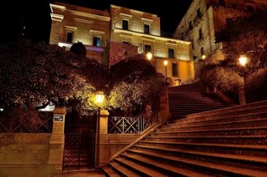 A nighttime view of a building with a staircase leading to a gated entrance.