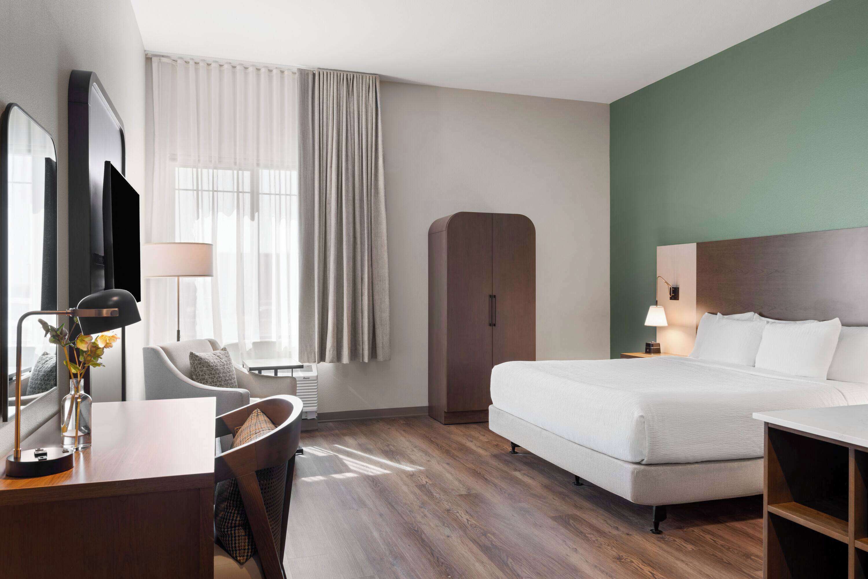 Una camera d'albergo con un letto, una scrivania, una sedia, un armadio e una finestra con tende.