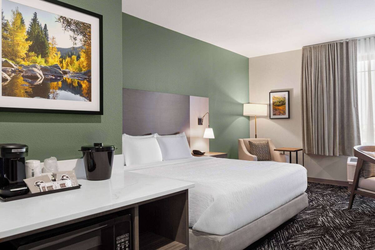 Une chambre d’hôtel avec un lit, un bureau doté d’une machine à café, une lampe et un tableau au mur.